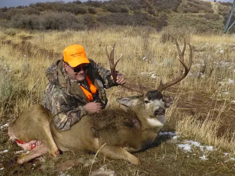 Hunter with a mule deer buck in the grass