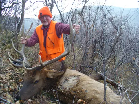Hunter in blaze orange with a bull elk on the ridge