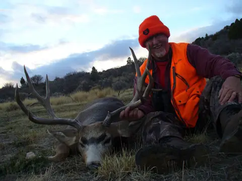 Hunter in blaze orange with a mule deer buck
